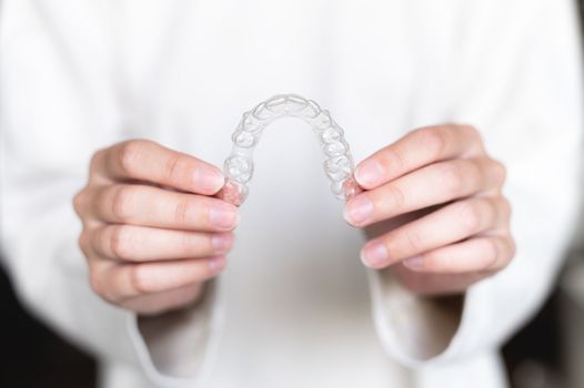 Close-up of a woman's hand holding invisible aligners for whitening and straightening teeth on a blurred background. Orthodontic treatment after braces. Dental health