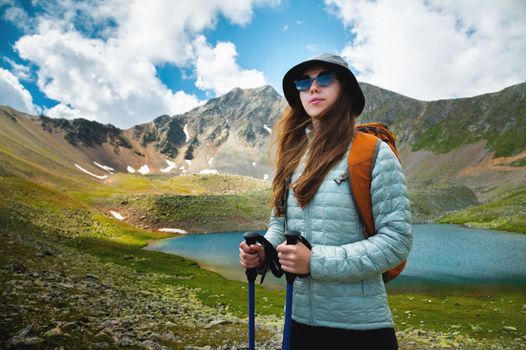 young woman stands on a rock and looks to the side, near a lake in the autumn mountains. Mountain lake and traveler with a backpack