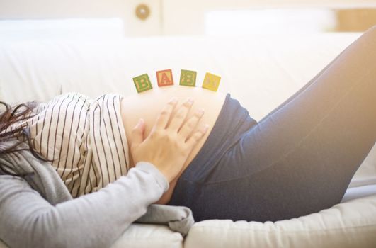 Love begins before birth. an unrecognizable young pregnant woman balancing wooden blocks on her tummy while relaxing on the sofa at home.