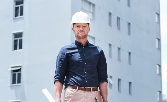 Always ready to help build your future with you. a mature male construction worker holding blueprints while standing outside a building.