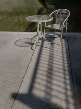 Sunbeam shine through the bridge and refect the white metal chair and the table with river view.