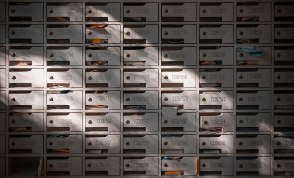 Beautiful sunlight shine on rows of white wooden mailboxes with keyholes for resident in condominium.