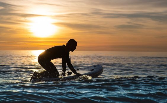 a sporty guy swims with a paddle on a sapboard in the sea under the beautiful sunset sun
