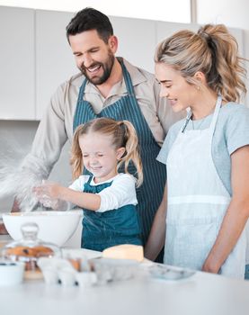 Happy parents baking with their daughter. Little girl making a mess with flour. Small, excited girl playing with flour. Mother and father watching their daughter while baking. Family baking together.