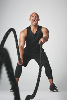 Battling the ropes. Studio shot of an athletic young man working out with battle ropes against a grey background.