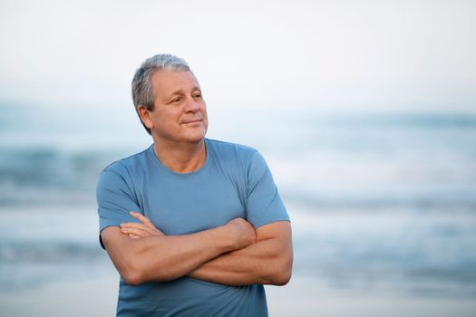 Cheerful retired man with crossed arms by the sea