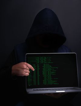 You could be the next victim. Portrait of an unrecognisable hacker holding up a laptop against a dark background.