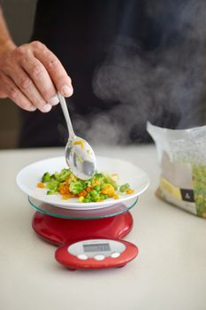 Vegetables are a must with every meal. Cropped image of a man spooning cooked vegetables onto a kitchen scale.