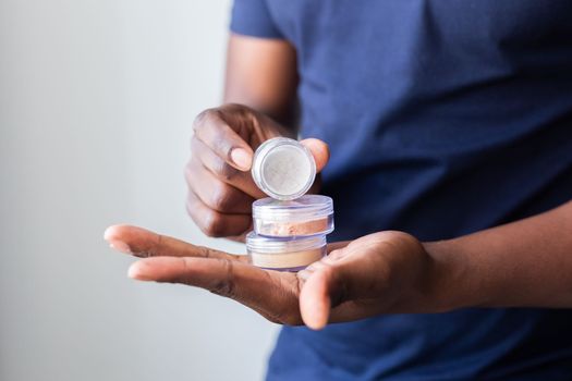 African american man holds mineral facial powder for perfect make-up for women - male make-up artist and cosmetic product concept