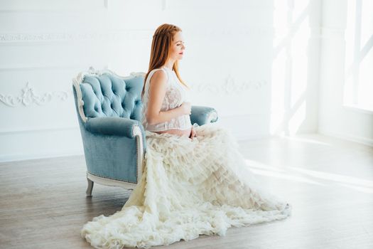 red-haired pregnant young girl in a blue armchair