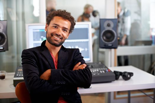 Hes made a name for himself in the biz. A handsome music producer sitting with arms folded in his studio.