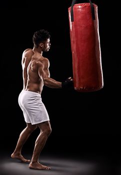 Strike while the iron is hot. Studio shot of kick boxer working out with a punching bag against a black background.