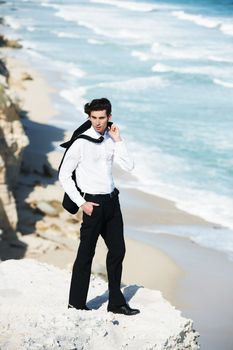 Getting away from the office. Handsome businessman standing on a cliff above the ocean with his jacket tossed over his shoulder.