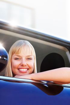 Happy blond woman sitting at the window seat of a car. Portrait of a smiling blond female sitting relaxed at the window seat of a car.