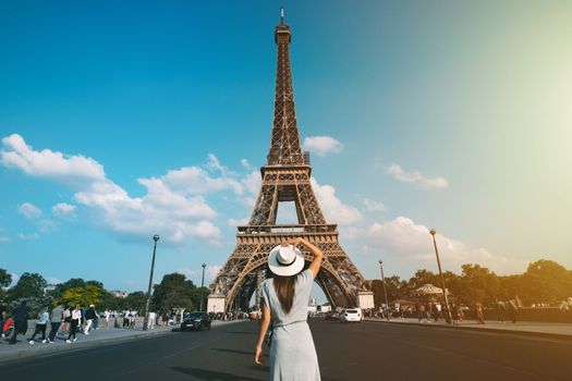 Rear view of woman tourist in sun hat standing in front of Eiffel Tower in Paris. Travel in France, tourism concept. Holiday or vacation in Paris