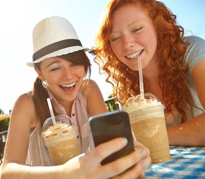 What a funny text. Two adolescent girls enjoying smoothies while texting on a cellphone.