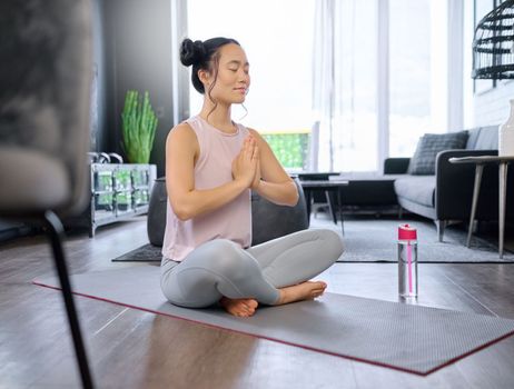 Prayer hands, yoga and meditation of Asian woman in home living room for mindfulness exercise. Zen chakra, pilates and female yogi training and meditating with namaste hand pose for relax and peace.