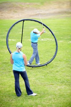 Your swing should stop when you get to here...Image of a male coach instructing his female student using a ring to adjust and correct her swing.