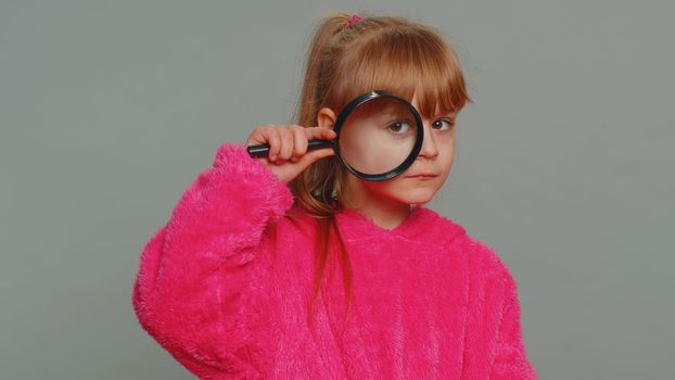 Curious preteen child girl kid holding magnifying glass near face funny eye searching analysing