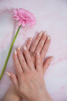 Hands of a woman with imperfect manicure with with pink gel polish and gerbera