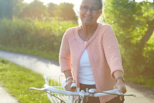 Summer biking. A lovely senior woman standing with her bike beneath a summer sun.