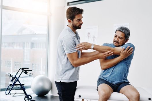 That shoulder still giving you issues. a young male physiotherapist helping a mature male patient with movement exercises at a clinic.