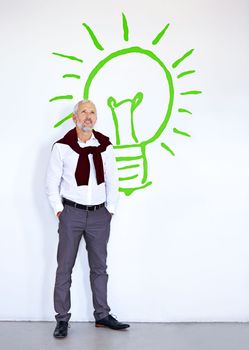 Coming up with bright new ideas. A mature businessman looking thoughtful while standing in front of a white wall with a lightbulb on it.