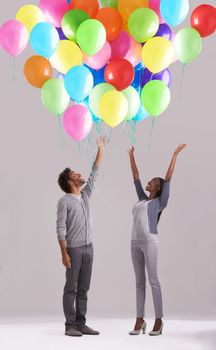 Let your dreams take flight. Studio shot of a young couple releasing a big bunch of balloons into the air.