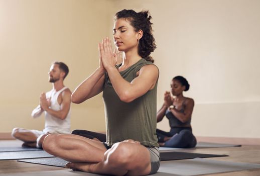 Peace begins within. Full length shot of a group of young people meditating and practicing yoga together inside a yoga studio