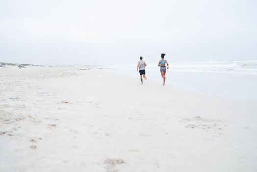 En route to better health and wellbeing. Rearview shot of a young couple running along the beach together.