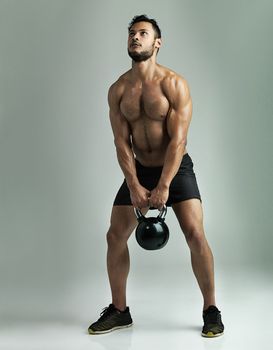Building his muscle definition. Studio shot of a young man working out with a kettle bell against a gray background.