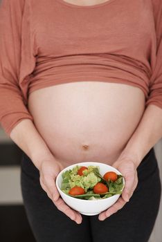 Just for the baby. a young pregnant woman holding a salad in the kitchen.