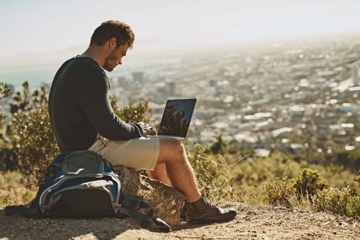 Starting a new blog on hiking. a young man using his laptop while sitting on a mountain top.