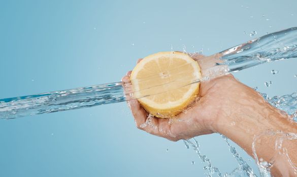 Water, splash and beauty with hands and lemon for health, wellness and hydration. Vitamin c, refreshing or nutrition with citrus fruits and model against blue background for natural, vitality or diet
