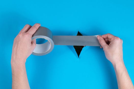 Woman sticking silver tape on a hole on a blue background.
