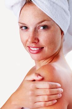 Smiling woman touching shoulder after a bath against white. Portrait of a female wrapped in towel and touching shoulders against white.