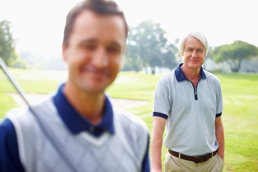 Senior golfer smiling. Portrait of senior man standing on golf course and smiling with son in foreground.