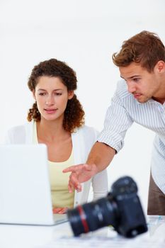 Business man and woman using laptop. Business woman using laptop with man pointing at the screen and camera in foreground