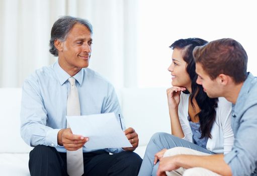 Mature advisor explaining financial plan to young couple. Mature advisor explaining financial plan to young couple at home.