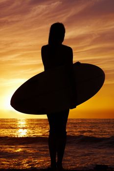Silhouette of a woman carrying a surfboard at sunset by sea. Full length silhouette of a woman carrying a surfboard at sunset by sea.