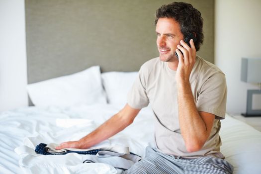 Man talking on cellphone. Mature man sitting on bed choosing tie and talking on cellphone.