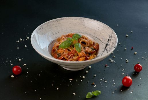 Penne pasta with tomato sauce, parmesan cheese and basil on a dark background. Top view with copy space.