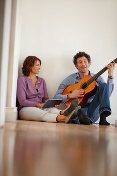 Keep calm and play guitar. a woman using her digital tablet while her husband plays the guitar.