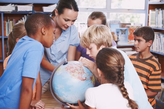 Getting to know the world. A young boy looking at a world globe as his classmates and teacher watch.
