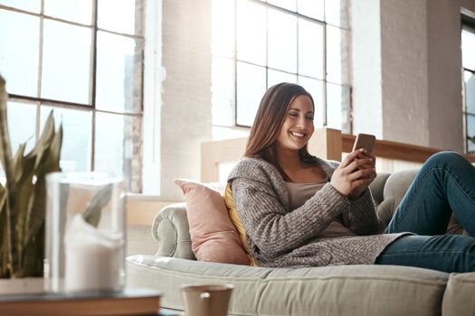 Happy, woman and phone for social media on a sofa, texting and chatting on dating app in her home. Girl, smartphone and text conversation in a living room, smile and relax while streaming and resting