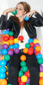Feeling whimsical. Attractive young hipster girl lying in a bath tub of colorful plastic balls.