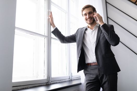 young successful businessman speaks on the phone in a jacket at the window in the office
