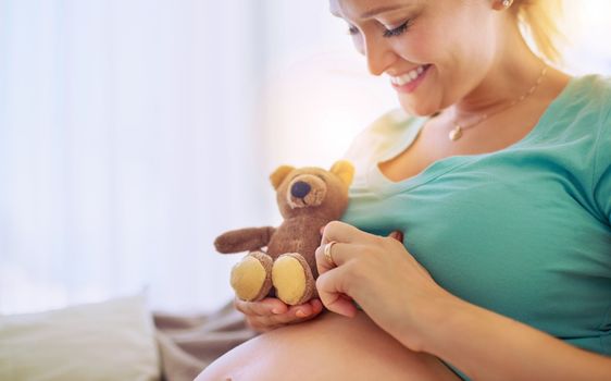 Youll be the babys best buddy, little teddy. a pregnant woman holding a teddy bear while relaxing at home.