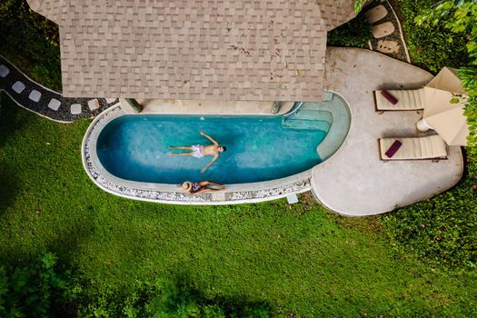 Drone view from above at a young couple of men and women at a swimming pool during a vacation