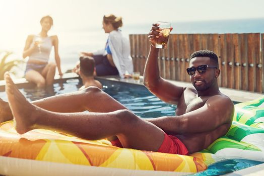 The coolest guy at the party. Portrait of handsome young man raising up his glass for a toast while relaxing in a pool outdoors with friends.